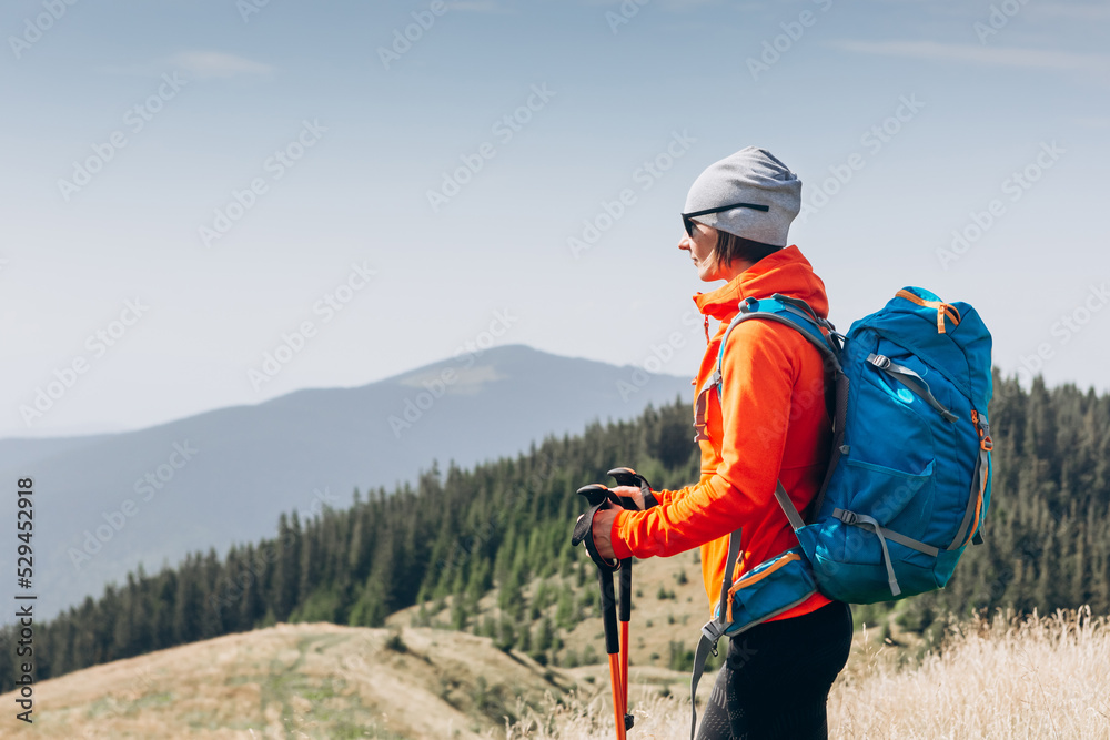 happy woman hiker standing on the top of mountain ridge against mountains, blue cloudy sky on background. Travel and active lifestyle concept