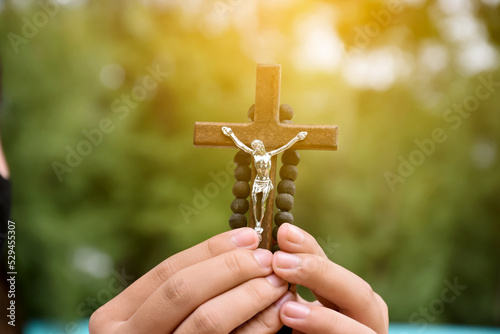 Obraz na plátně Wooden cross and wooden rosary are held in hands of young asian Catholic prayer while praying in the temple park area