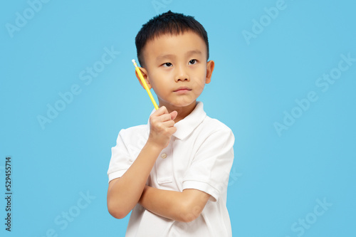 Smart kid crossing arms and thinking, looking up and holding pencil on blue background