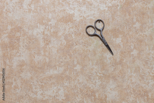 Manicure scissors hang on a small nail driven into the wall. Wall with wallpaper inside the house.