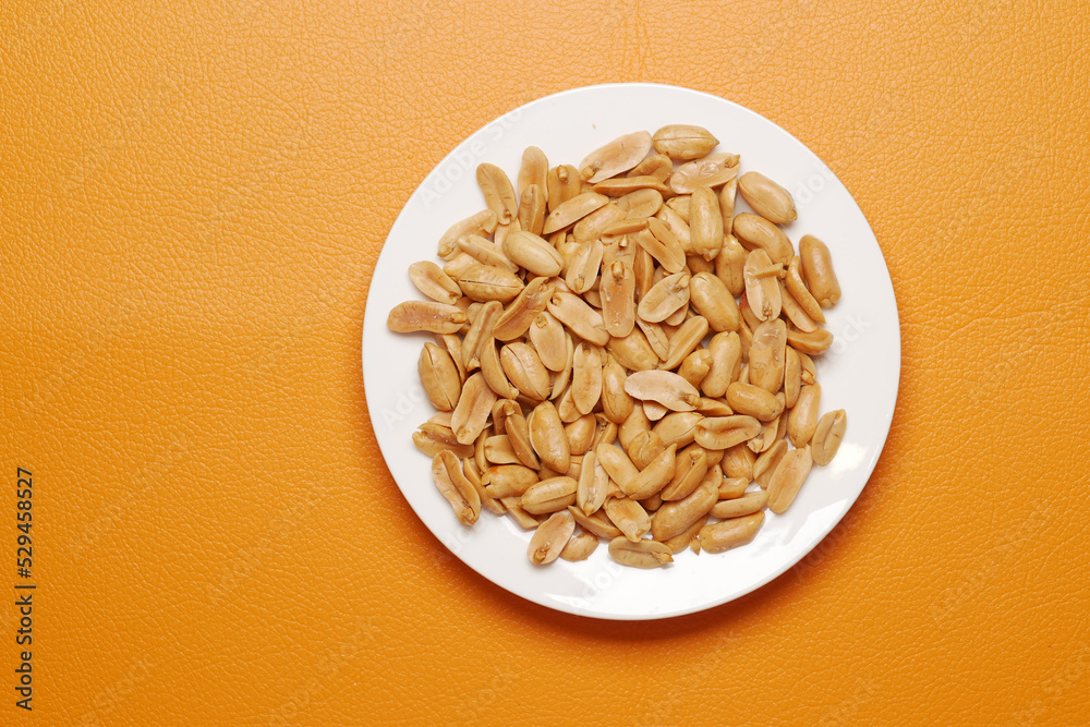 Peeled peanuts on a plate on orange background Peeled peanuts on a plate on orange background
