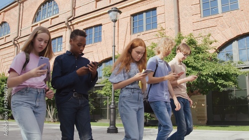 Group of multinational college students obsessed with smartphones walking outdoors