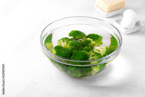 Blanching broccoli florets in cold water in glass bowl on white table. Cooking ingredient for salad, pie or side dish