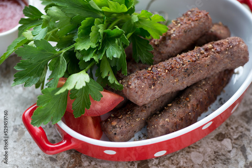 Red serving pan with bbq serbian cevapi or cevapcici sausages and fresh parsley, closeup, selective focus photo