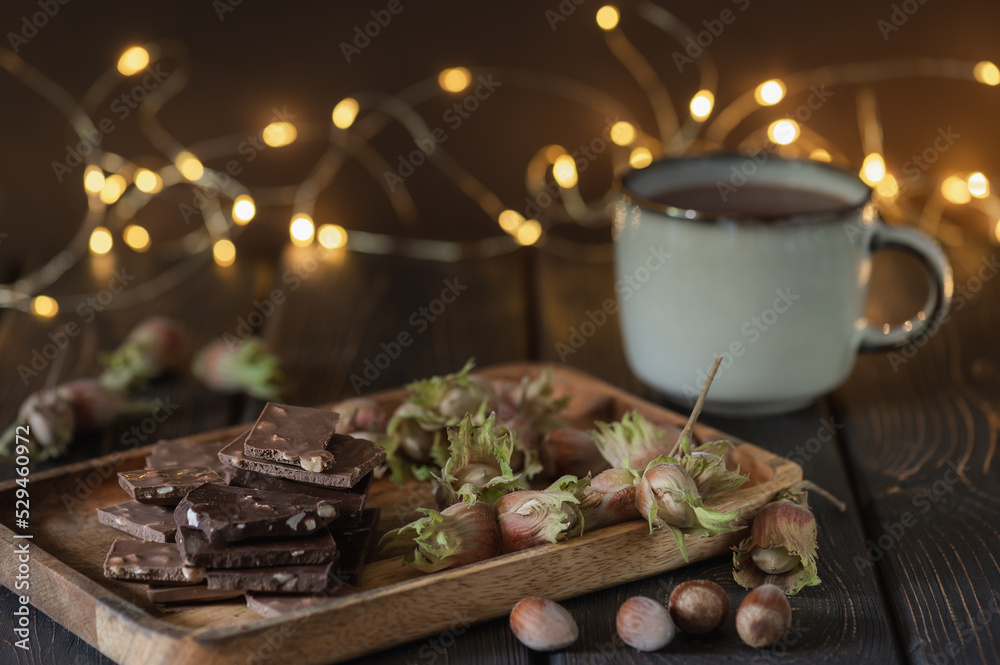 Pieces of chocolate with nuts, hazelnuts and a mug with cocoa on a dark background with bokeh.