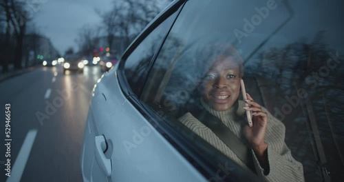 Young black woman is on her phone talking to a friend while beeing on the backseat of a taxi