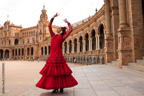Beautiful teenage woman dancing flamenco in a square in Seville, Spain. She wears a red dress with ruffles and dances flamenco with a lot of art. Flamenco cultural heritage of humanity. photo