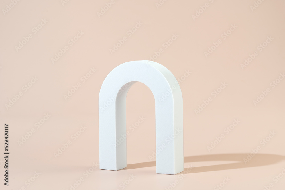 A white geometric shape in the form of the arch standing on a beige background A white geometric shape in the form of the arch standing on a beige background