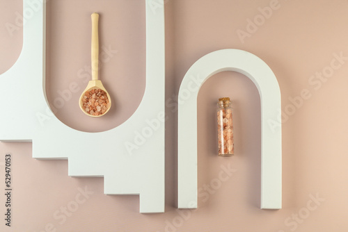 A pink sea salt in mini glass bottles lying betwen geometric shapes on a beige background, minimalism concept of body care photo