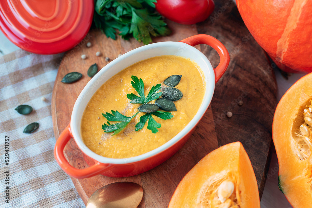 Pumpkin soup in a saucepan with parsley and pumpkin seeds on cutting board. Autumn food, top view Pumpkin soup in a saucepan with parsley and pumpkin seeds on cutting board. Autumn food, top view