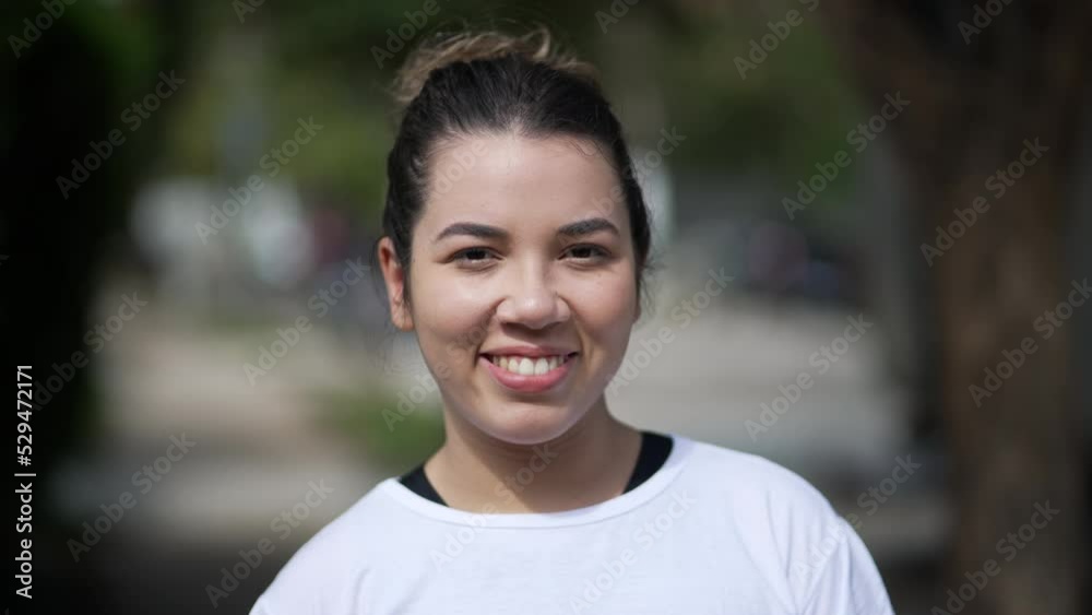 Happy young woman portrait face closeup standing outside looking at camera. Casual female person in 20s stands outdoors Happy young woman portrait face closeup standing outside looking at camera. Casual female person in 20s stands outdoors
