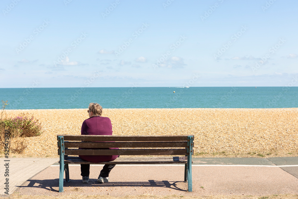  Woman Relaxing On A Park Bench On A Clear Summers Day, looking out towards the sea