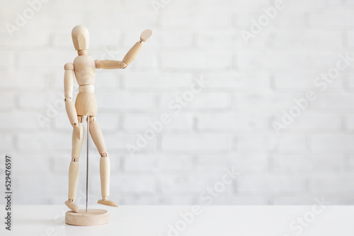 wooden human figure showing hello sign over white brick wall background