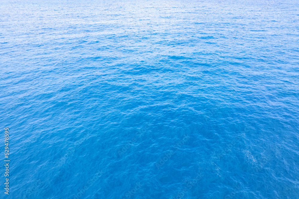 Obraz premium Aerial view of a blue sea water background and sun reflections. Aerial flying drone view and shadow clouds on sea surface,water texture on ocean, Aerial photography. Birds eye view. Sea