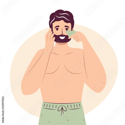 Skincare routine concept. Happy young man doing lymphatic face massage with jade face gua sha stone scraper.Male Facial yoga, handsome bearded male enjoying skincare procedure. Men hygiene.
