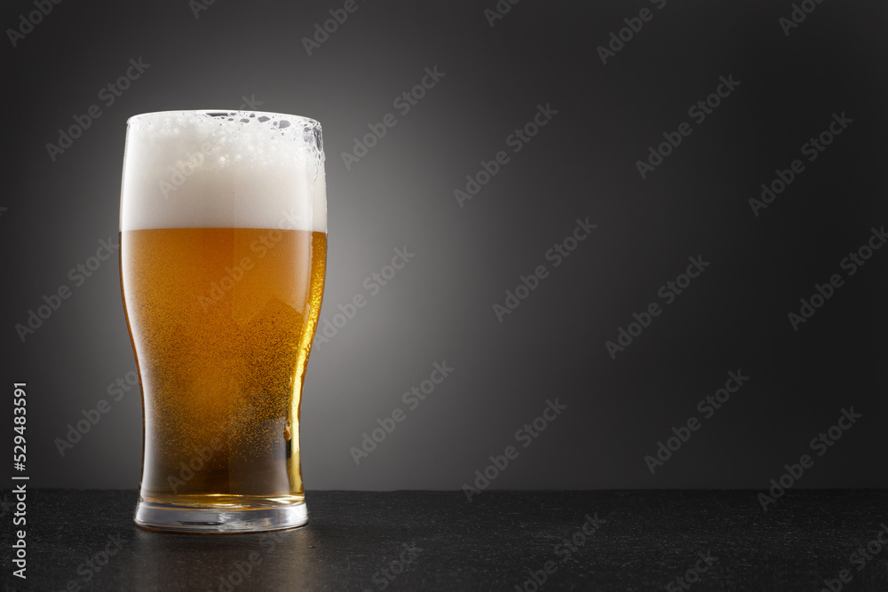 Draught beer in glass on a granite stone with copy space. Full glass of fresh golden and cold beer on dark gray background. Selective focus