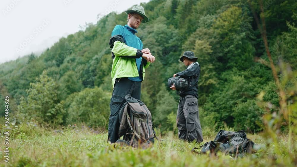 Concentrated tourist couple take off his jacket and are going to pitch a tent while standing in the mountains Concentrated tourist couple take off his jacket and are going to pitch a tent while standing in the mountains