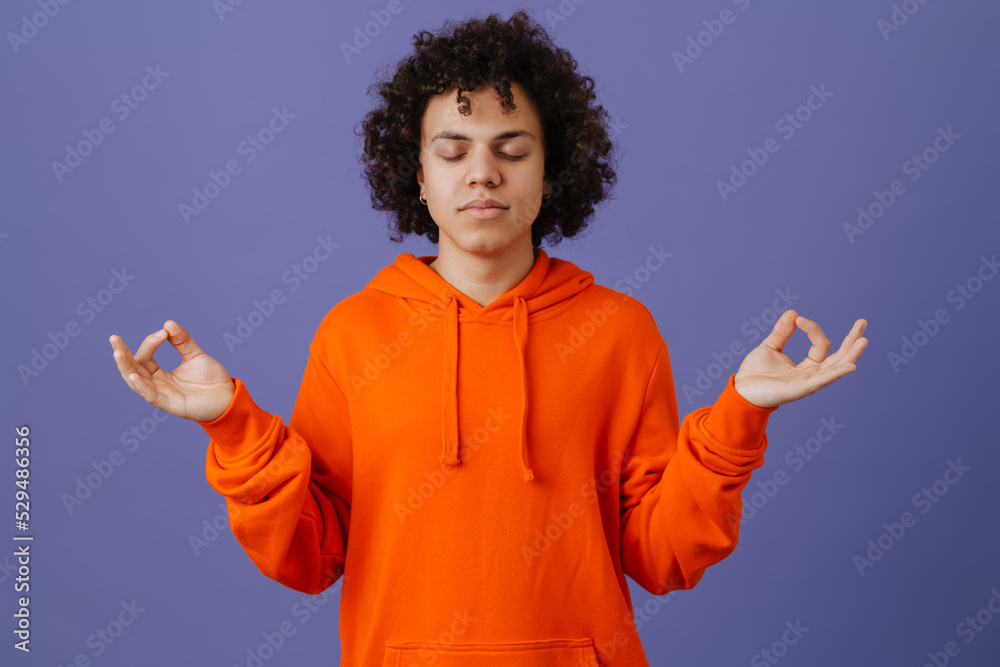 Young curly man wearing hoodie gesturing while meditating