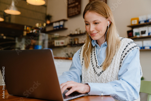 Blonde white woman listening music while working with laptop at cafe