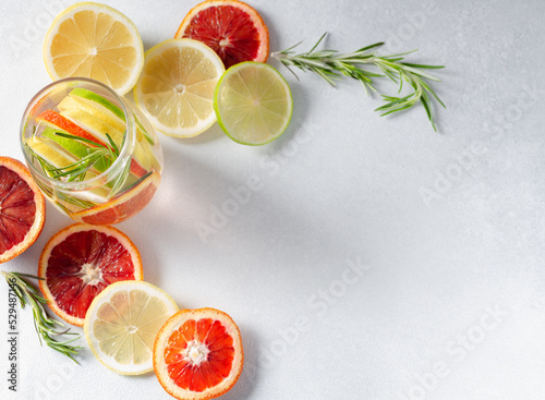 Mineral infused water or mocktail in a glass with lemon, lime, red orange and rosemary on white background  with copy space photo