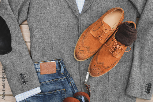 A pair of brown suede derby shoes, blue jeans, leather and bag belt with grey tweed blazer. Casual business outlook. Top view.