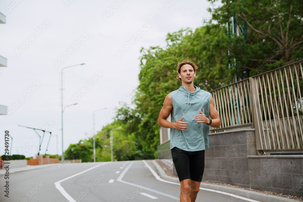 Young handsome athletic long-haired man in headphones running outdoors Young handsome athletic long-haired man in headphones running outdoors