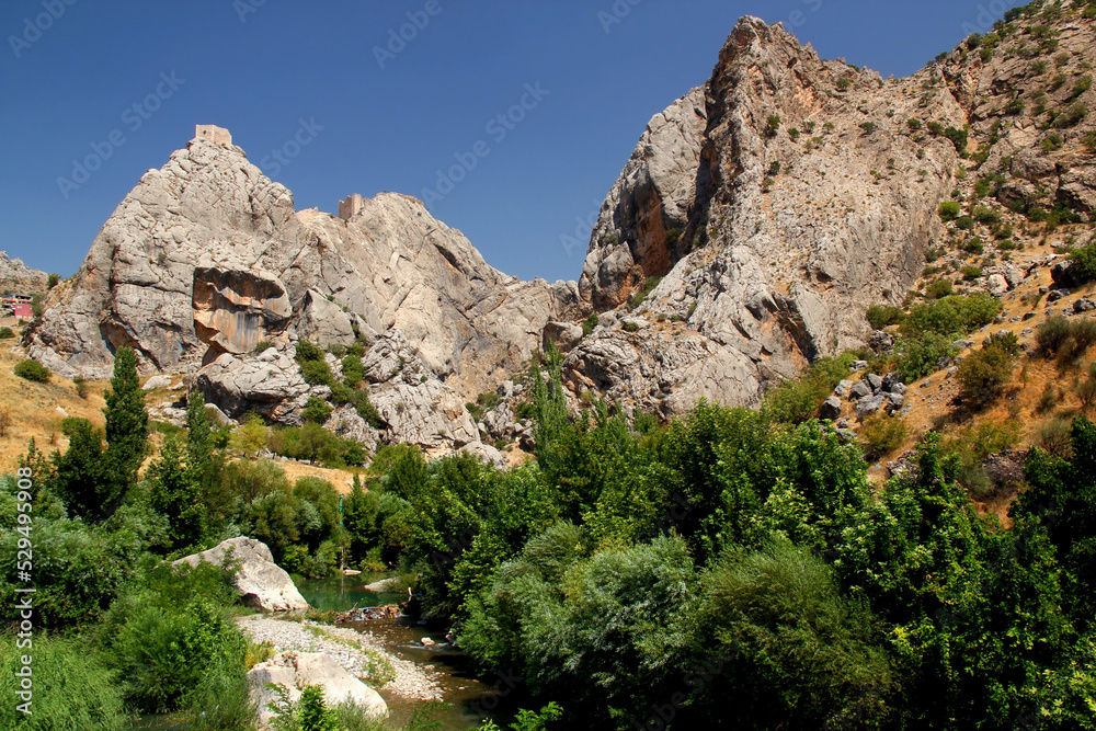 A landscape with a stream, a rock and the ruins of the old castle of Kahta on it near the ancient city of Arsameia in Southeast Turkey