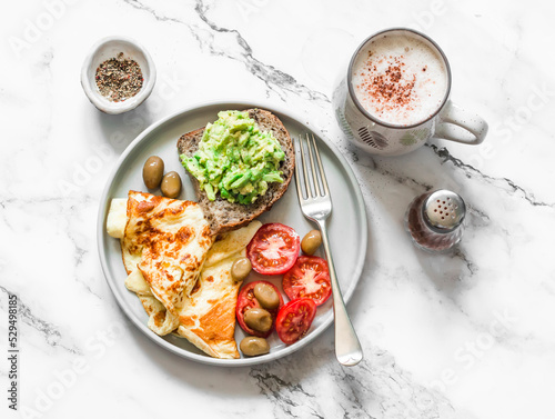 Homely cozy breakfast table - omelette, vegetables, avocado toast and cappuccino on a light marble background, top view