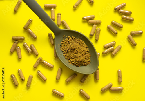 kratom pills composition on yellow background with kratom filled spoon, top view, flat lay