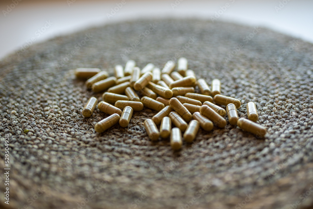 handful of green kratom pills capsules laying on wicker surface, selective focus handful of green kratom pills capsules laying on wicker surface, selective focus