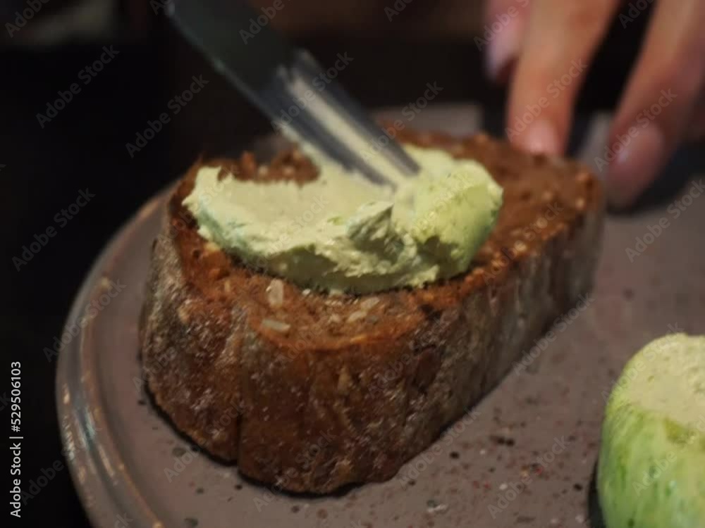 Woman spreading green butter on slice of brown bread on the gray plate. Woman spreading green butter on slice of brown bread on the gray plate.