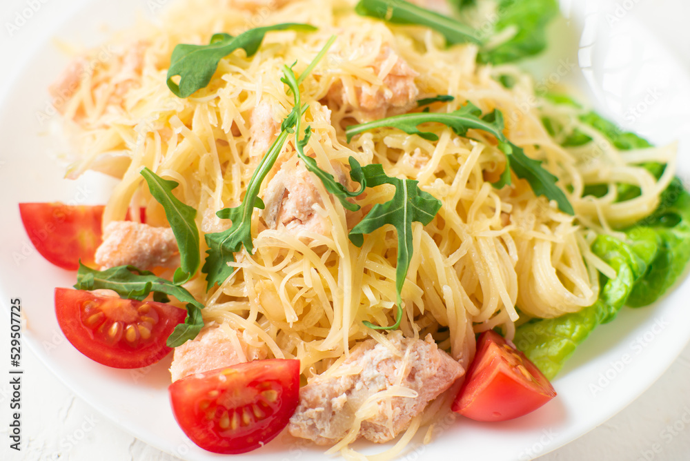 Spaghetti with salmon, cheese on a lettuce salad sprinkled with arugula and cherry tomatoes close-up. Spaghetti with salmon, cheese on a lettuce salad sprinkled with arugula and cherry tomatoes close-up.