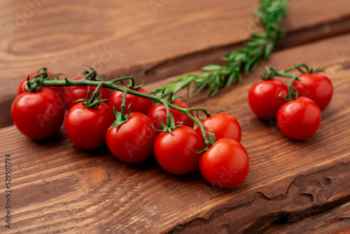 Cherry tomatoes and rosemary on a wooden background. Fresh tomato branch. Vegetarian food. © Konstiantyn Zapylaie