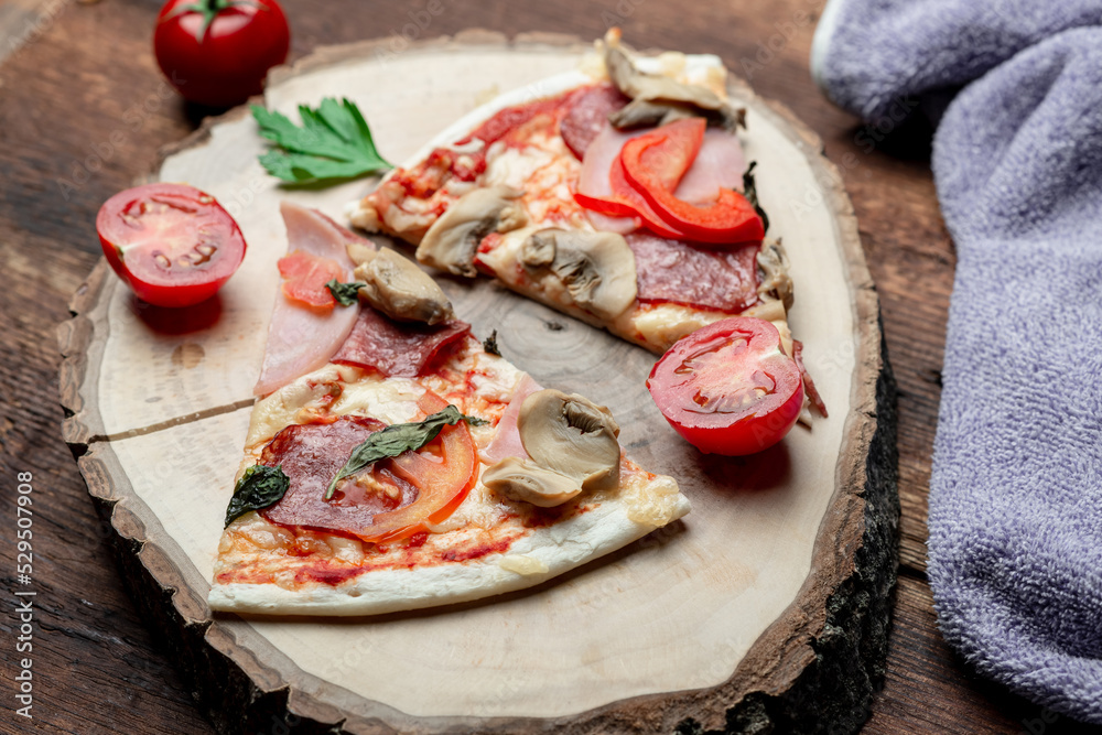 Pizza with ham and bacon, mushrooms and tomatoes on a slice of wood on a brown wooden background. Pizza with ham and bacon, mushrooms and tomatoes on a slice of wood on a brown wooden background.
