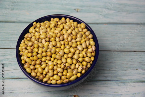 Yellow Ball Beans (Phaseolus vulgaris) in a blue bowl, isolated, on a wooden table, top view.