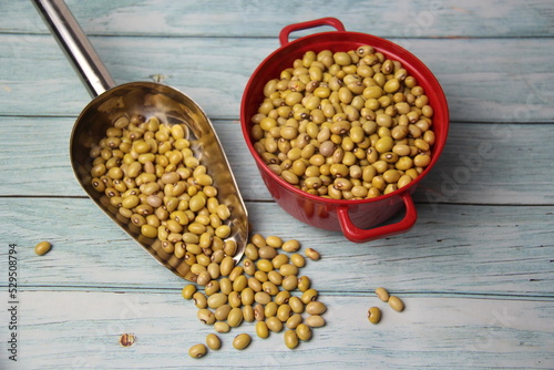 Yellow Ball Beans (Phaseolus vulgaris) in a stainless steel measuring spoon and red pot on a wooden table, top view.