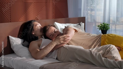Diverse male homosexual couple lying in bed together and hugging photo