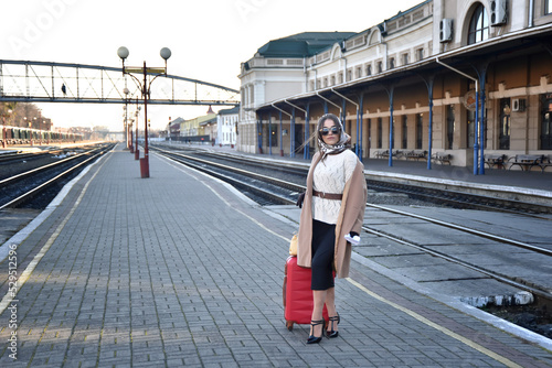 a young brunette with a scarf on her head in dark glasses and high heels is waiting for the arrival of a train on the railway