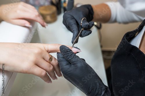 Manicure salon master removes cuticles with nail scissors. Woman getting nail manicure. Professional manicure in beauty salon. Hygiene and care for hands.
