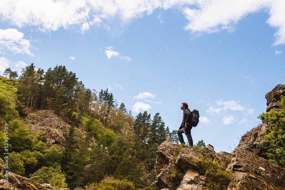 man with large backpack standing on top of a rock contemplating the forest and mountain landscape while taking a break on his hiking trail