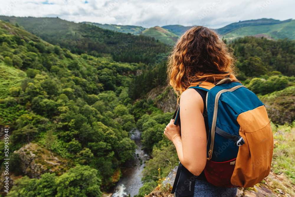 Woman from the back with a backpack contemplating the landscape of a river valley during a day of trekking. weekend outdoor activities concept