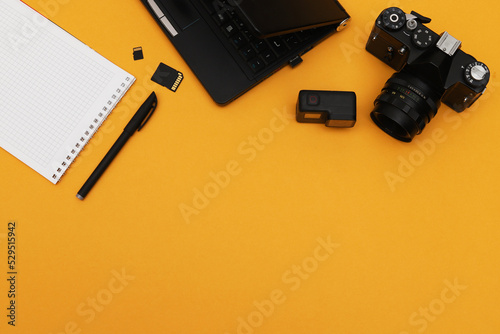 Top view of photojournalist concept with film camera, notepad and action camera on orange background. Office tools.