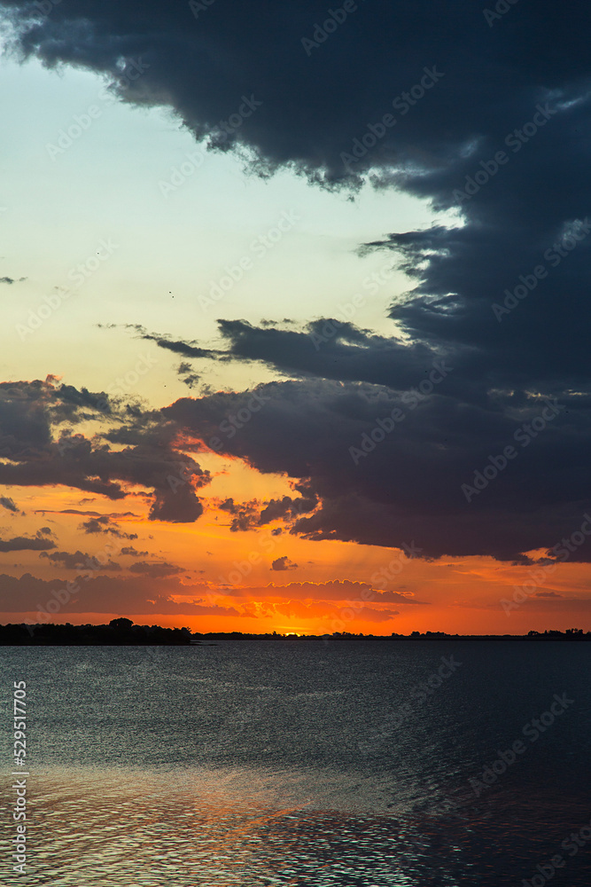 Sunset at the lagoon. The sky is orange and the lagoon marks the horizon line. Cloudy sky.