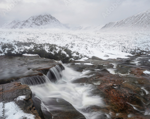 Majestic Winter landscape image of River Etive in foreground with iconic snowcapped Stob Dearg Buachaille Etive Mor mountain in the background
