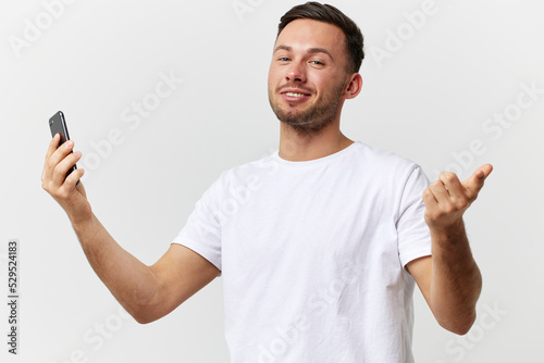 Cheerful smiling tanned handsome man in basic t-shirt talk by video call look at camera posing isolated on over white studio background. Copy space Banner Mockup. Distance online communication concept