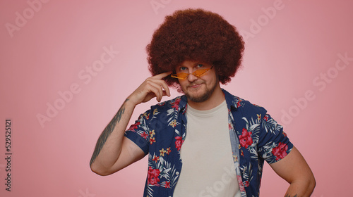 Playful happy bearded adult man 30 years old wearing yellow sunglasses blinking eye looking at camera with toothy smile, winking and flirting expressing optimism. Young guy boy on pink background