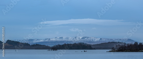 Beautiful landscape image of Loch Lomond and snowcapped mountain range in distance viewed from small village of Luss