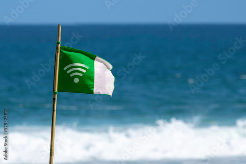 bandeira verde com símbolo de wi-fi, com mastro de bambu, sinalizando cobertura de internet e ao fundo mar e ondas estourando e céu azul. photo