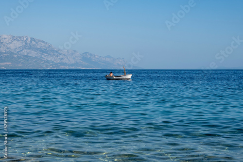 Man in the motor boat slowly passing over calm Adriatic sea, off the coast of Mimice, Croatia with intimidating Biokovo mountain rising in the distance above the shoreline