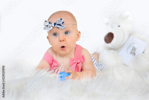 Cute baby girl in striped dress and pale blue headband lying on on a white fur blanket.